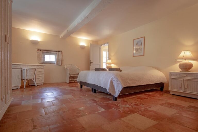 one bedroom of the two, with a double bed, terracota tiles on the ground and 2 bedside table